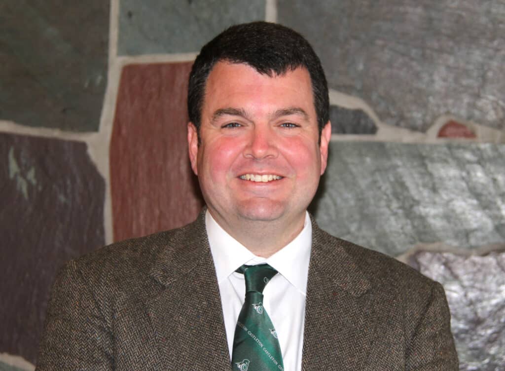A man with dark hair in a suit and tie smiles at the camera.