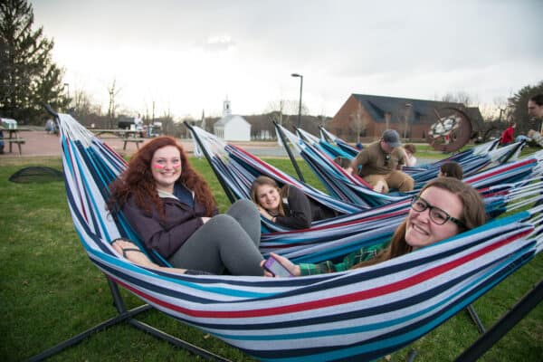 Group of smiling female students hang out in hammocks on the green on the Randolph Center campus