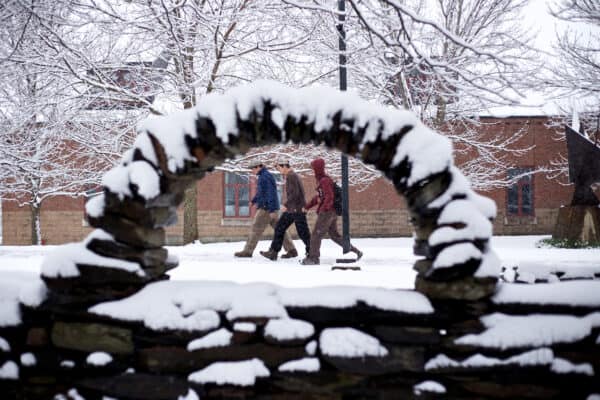 Three students walk in the snow in front of Clarke Hall