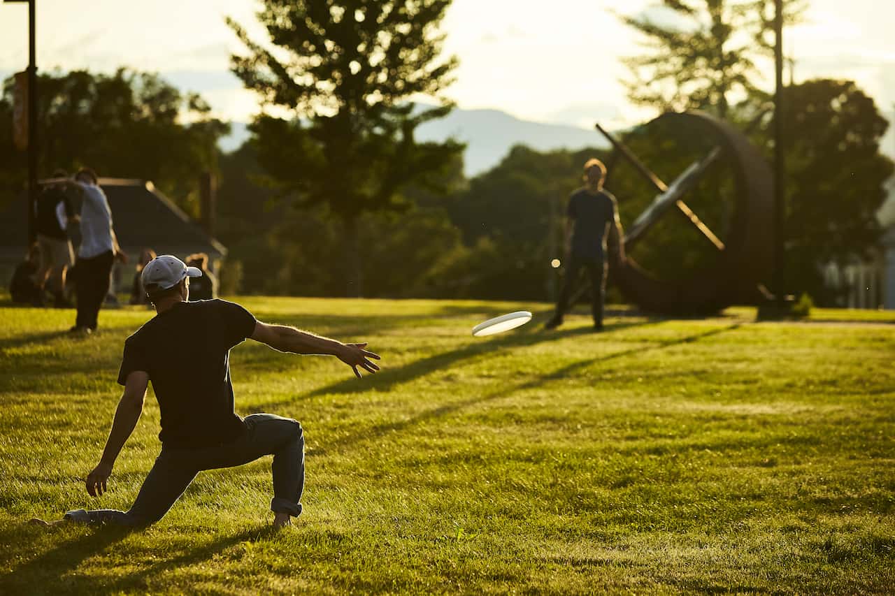 Students play frisbee on the green during sunset