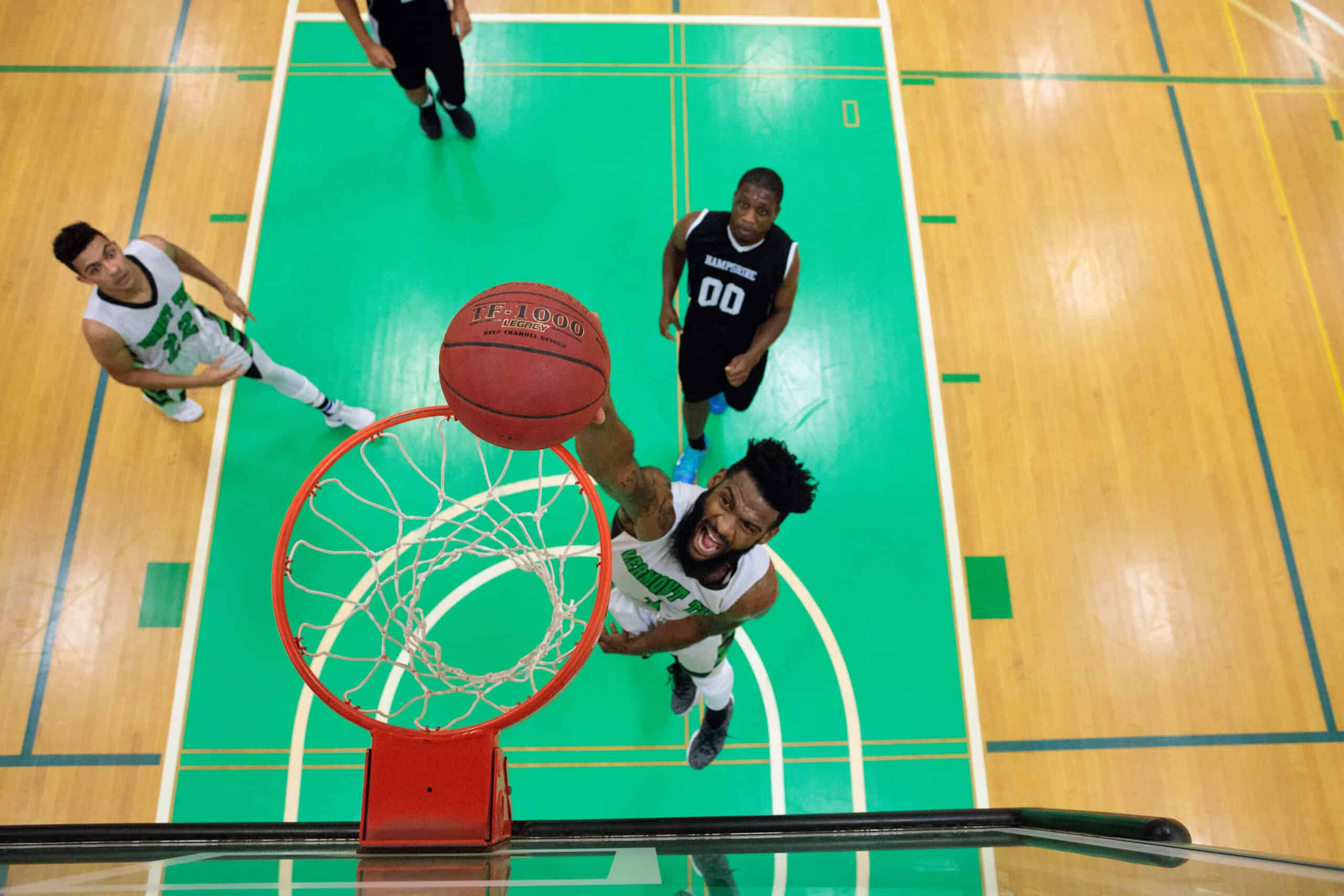 A downward facing picture of a man with a beard dunking a basketball into a basket.