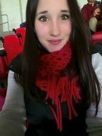 A selfie of a dark haired young woman in a black vest and red scarf.