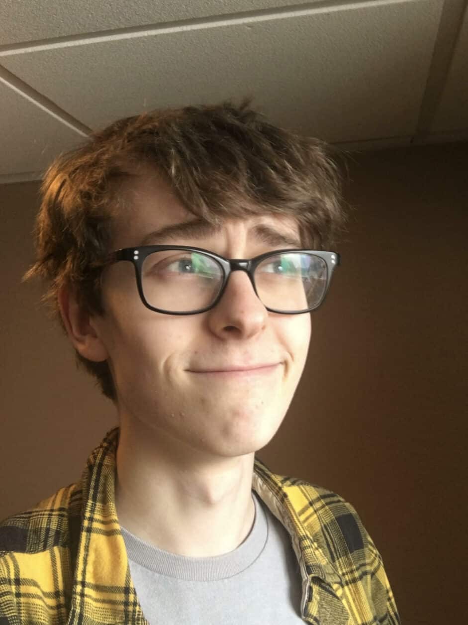 A young man in yellow plaid smirks and takes a selfie.