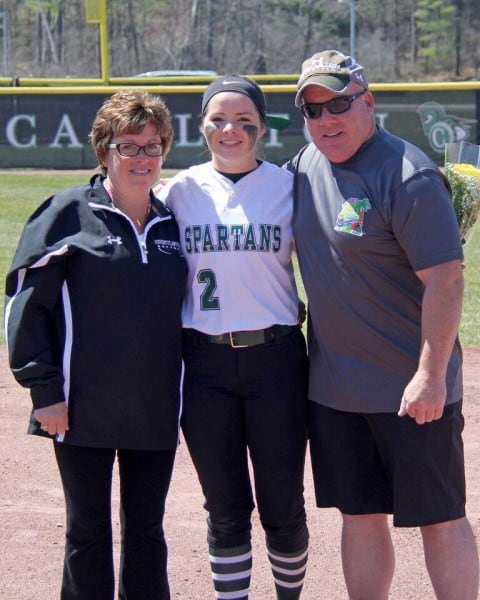 A photo of a girl in a sports uniform posing for a photo between two parental figures.