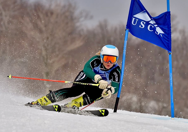 A Vermont State alum ski racing down a snowy slope.