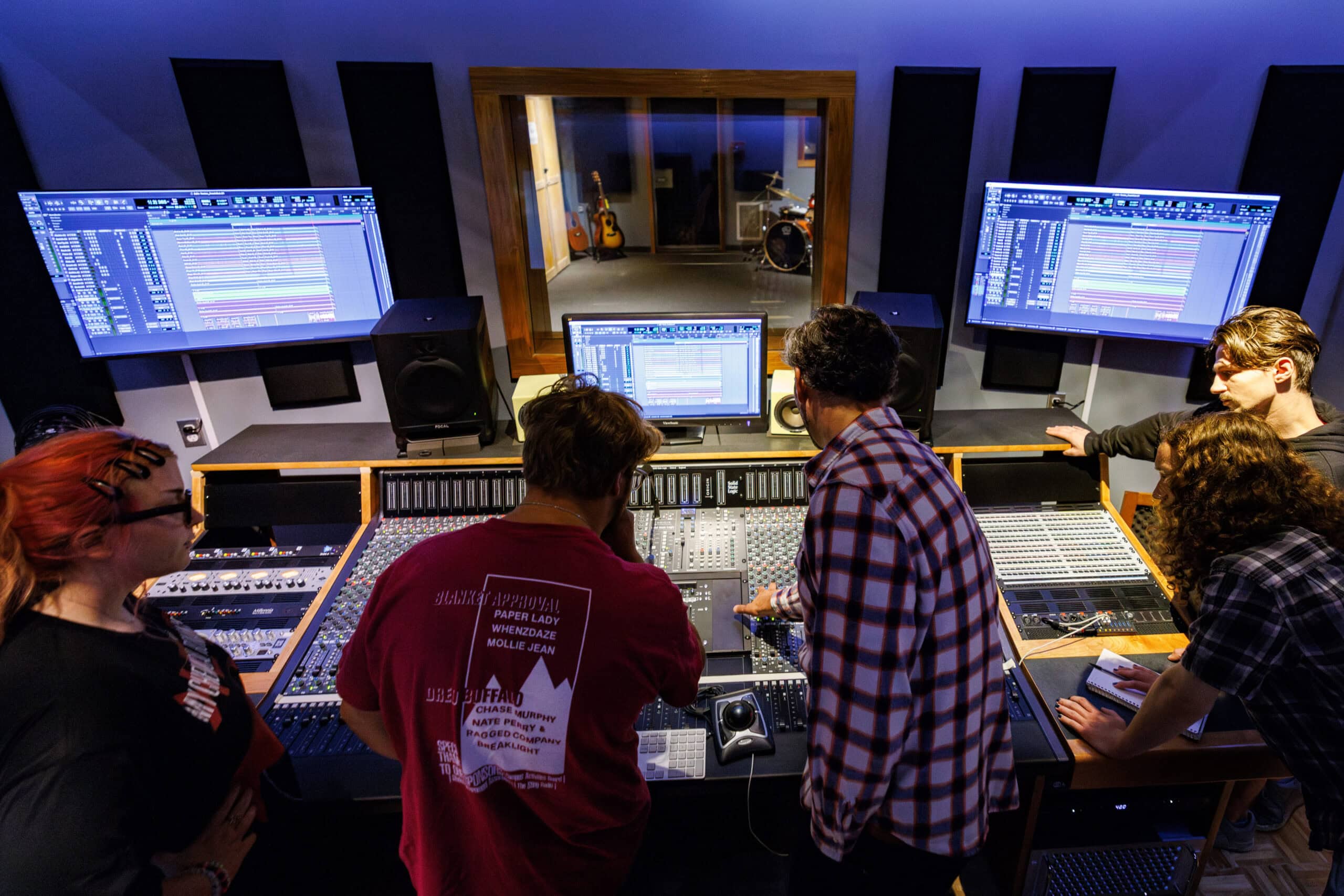 A group of students with their backs to the camera are leaning over a music recording console