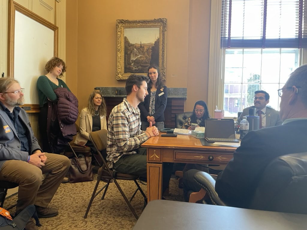 Carson Zundel sitting at a conference table with fellow students and legislators at the Vermont Statehouse