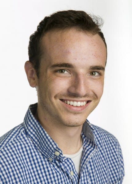A photo of Peter Marcano, a young man with short brunette hair wearing a blue and white checkered shirt smiling in front of a white background