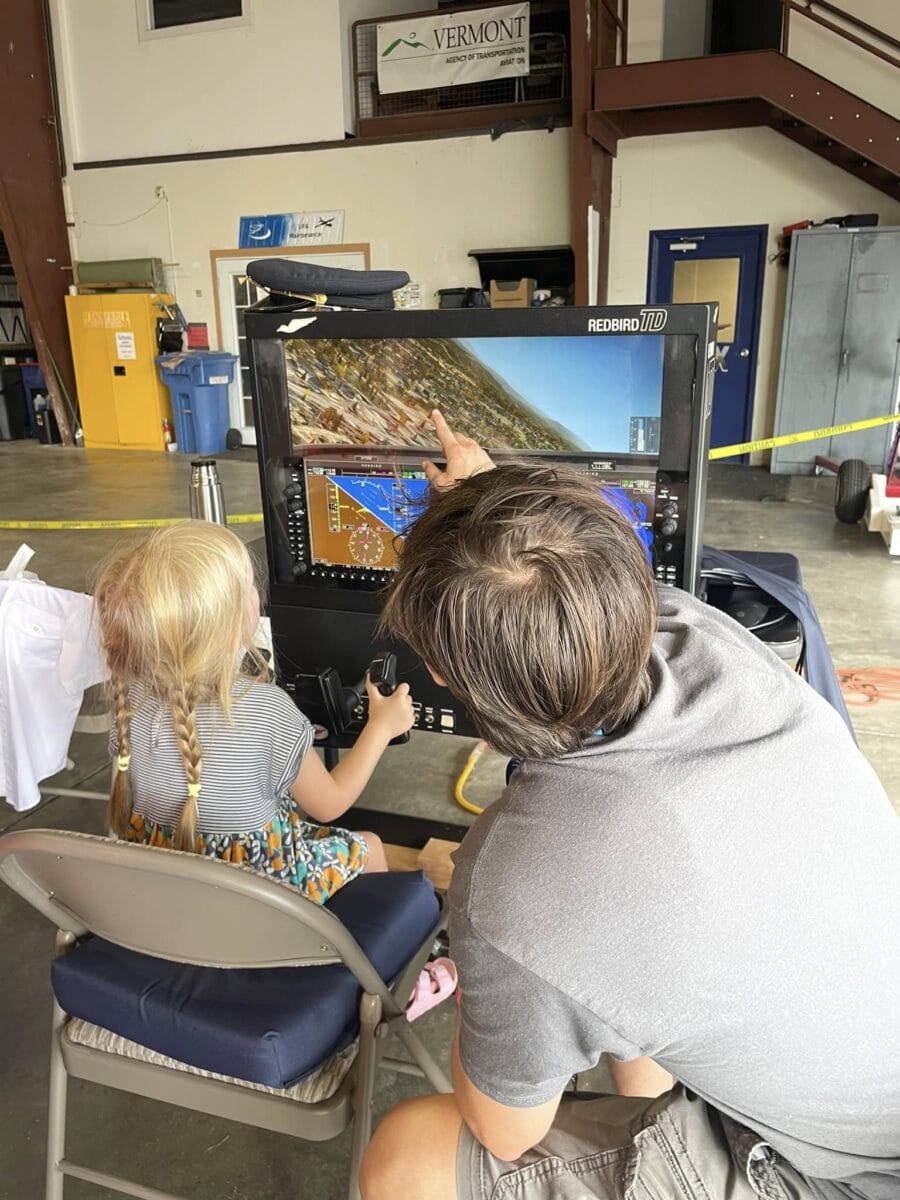 A pilot student from VTSU teaching a young girl how to use a flight simulator