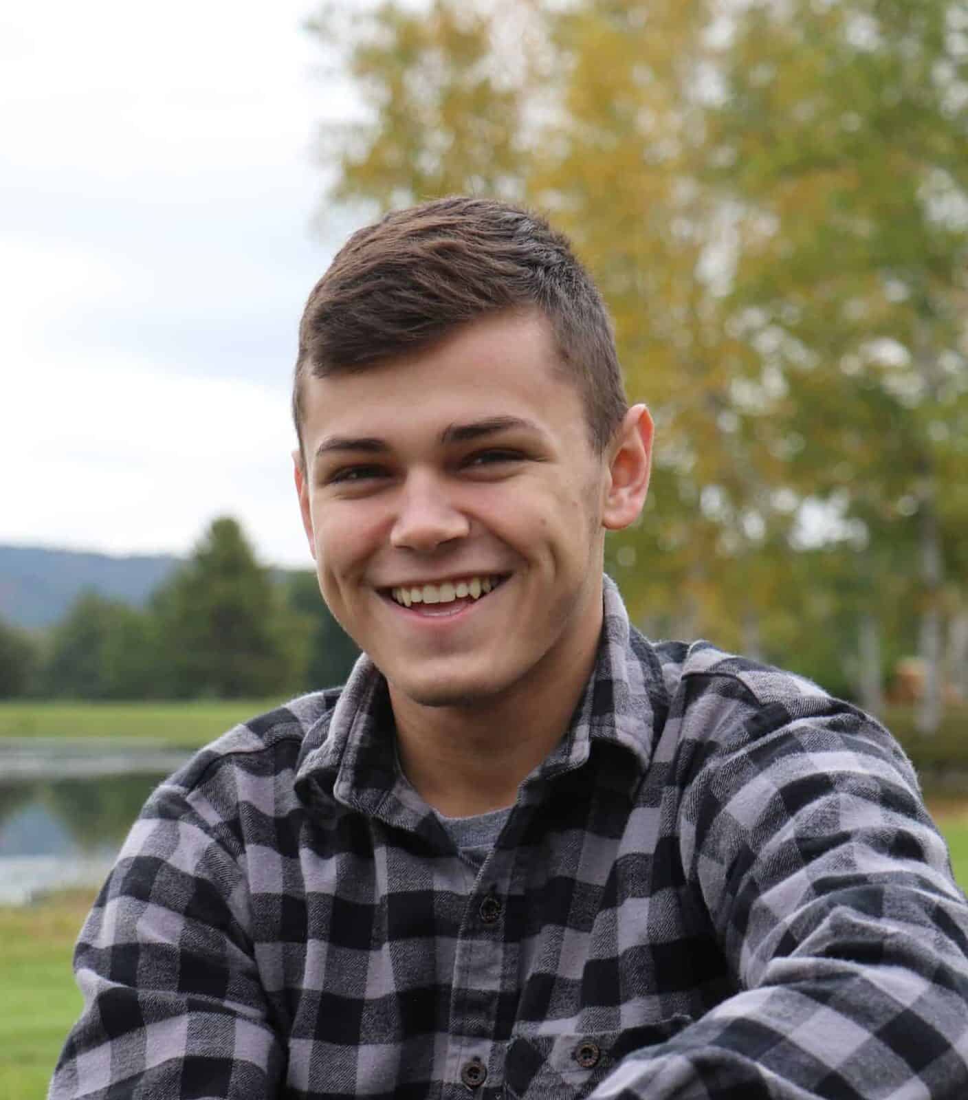 A photo of a young man smiling at the camera wearing a flannel shirt.