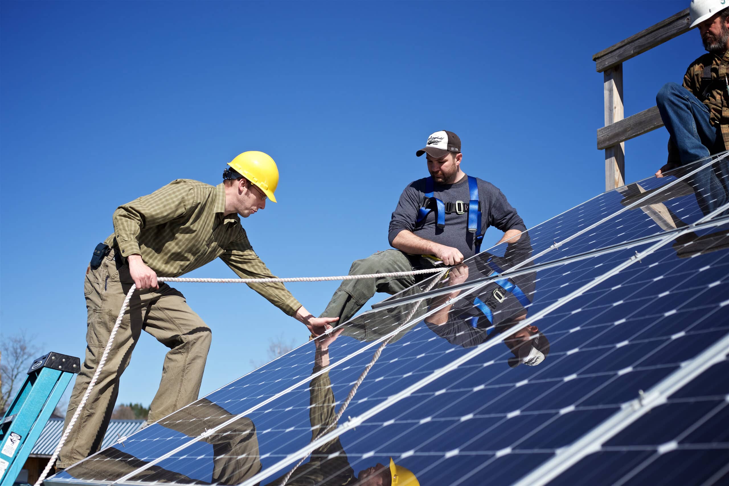 Two men stand on the side of a roof installing solar panels as part of the Vermont State University Renewable Energy program.
