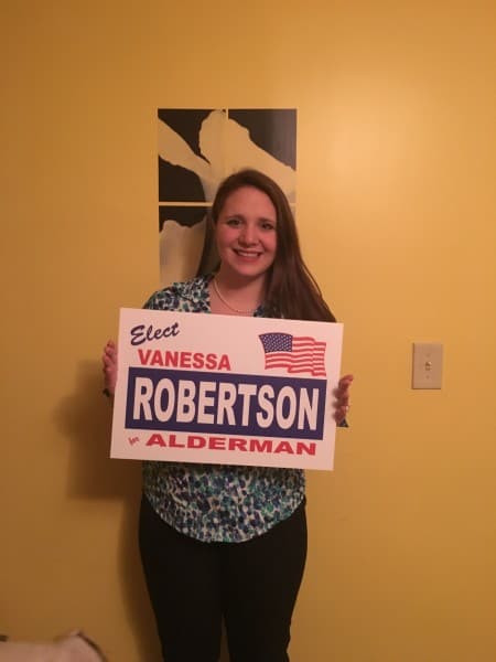 A woman holds up a political sign and smiles at the camera.