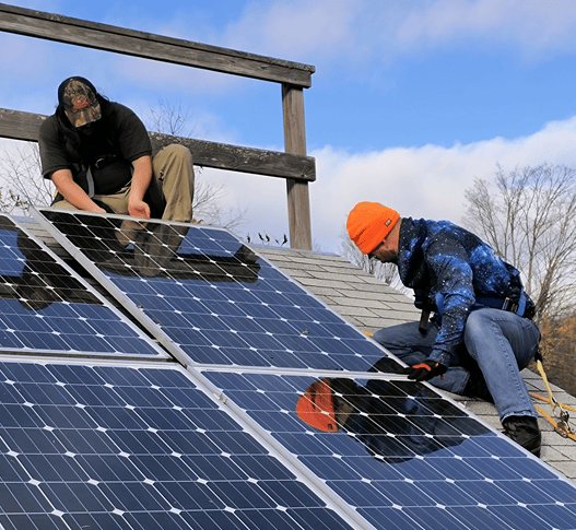 Two men from Vermont State University working on solar panels on a roof.