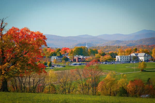 A scenic fall photo overlooking a cluster of buildings, mountains and farmlands.