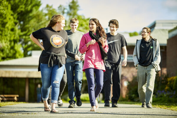 A group of five young people walking on a pathway towards the camera, talking to each other.