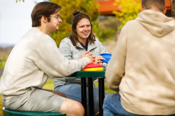 A young woman sits at a picnic table with a young man, frisbees sit on the table in front of them.