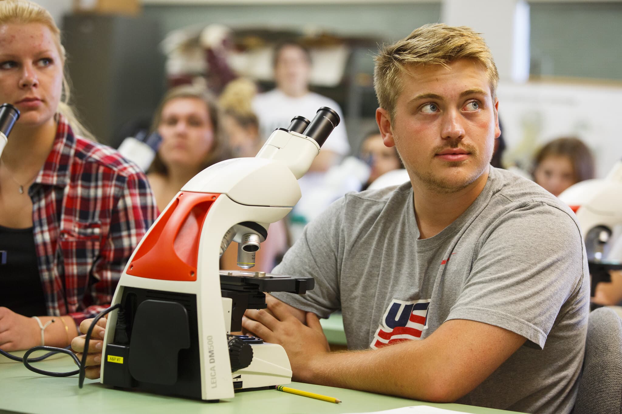 A blond man sits at a microscope in a Vermont State University lab.