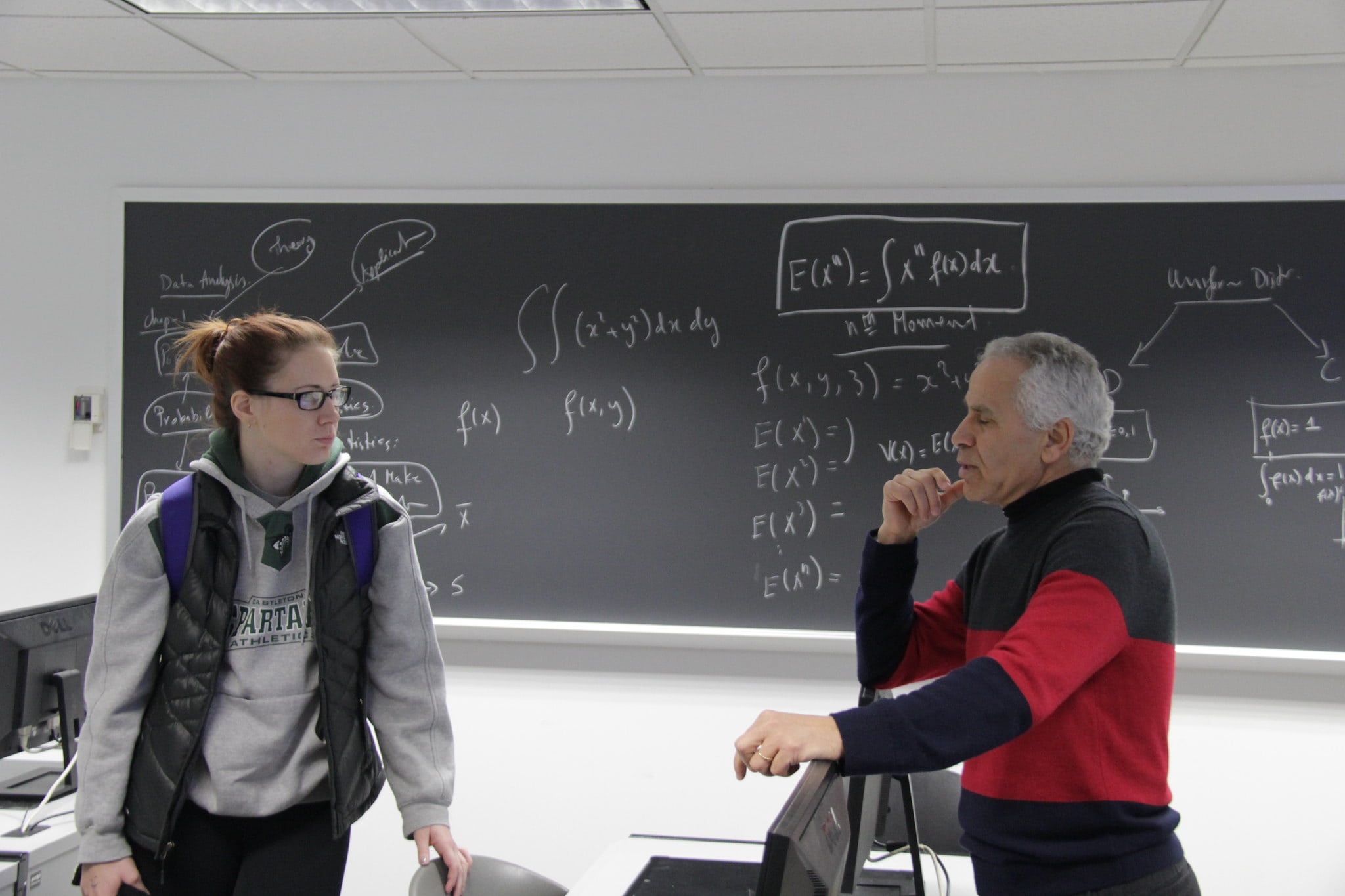 Two individuals standing in front of a blackboard in conversation at Vermont State University.