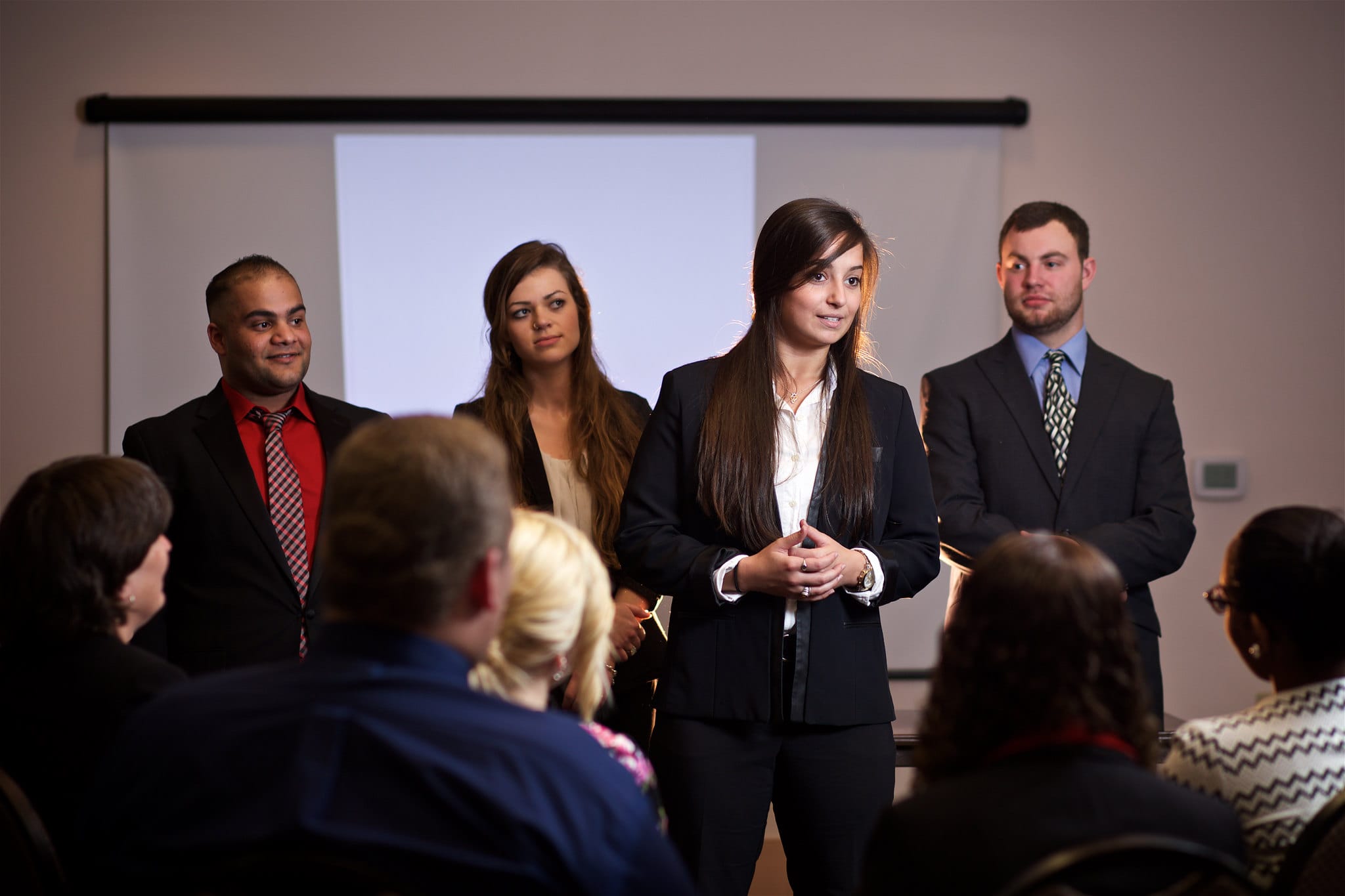 A woman is standing addressing a group of people while three others stand behind her.