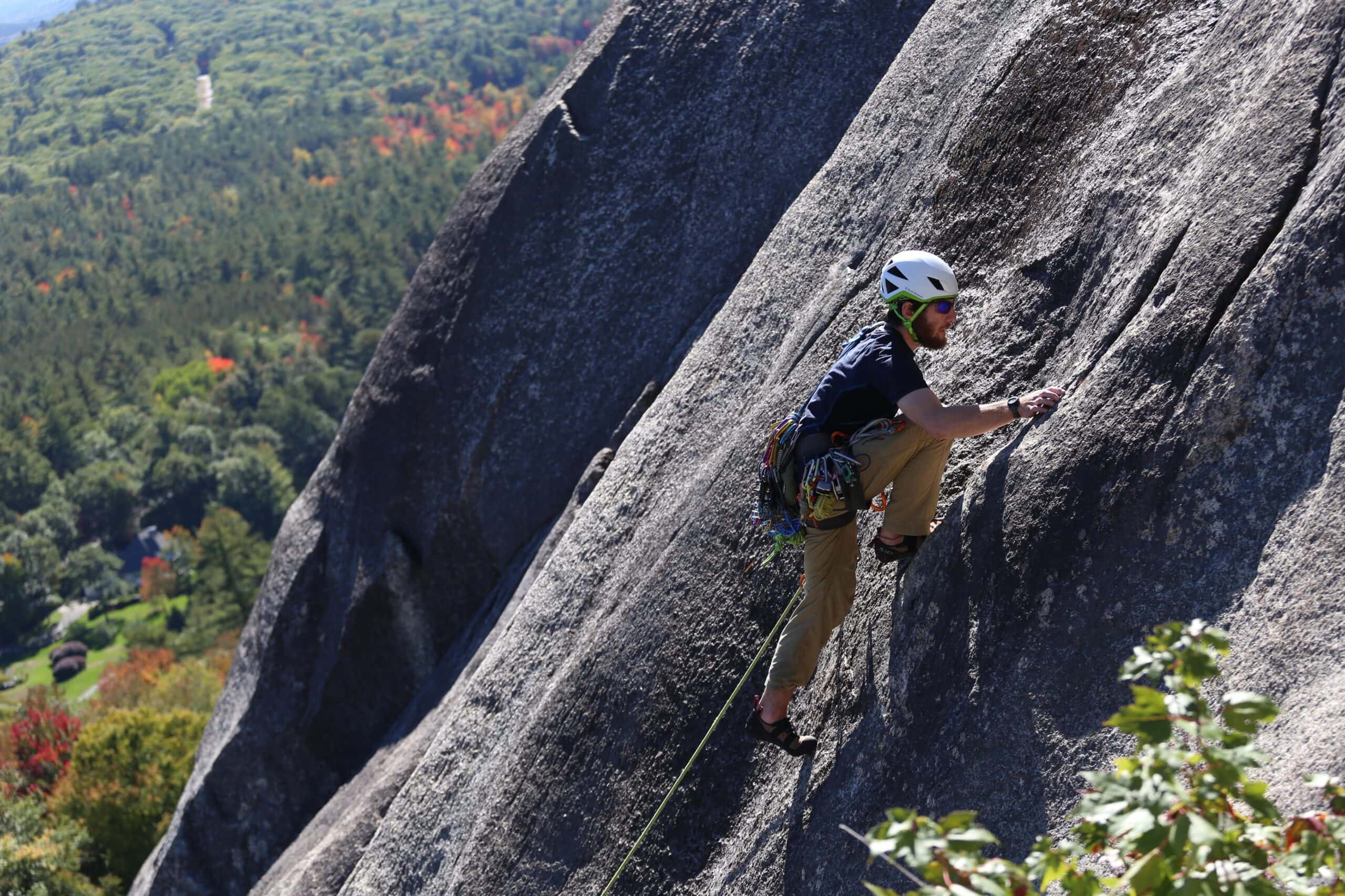 A person in a helmet and harness scales the side of a high rock face.