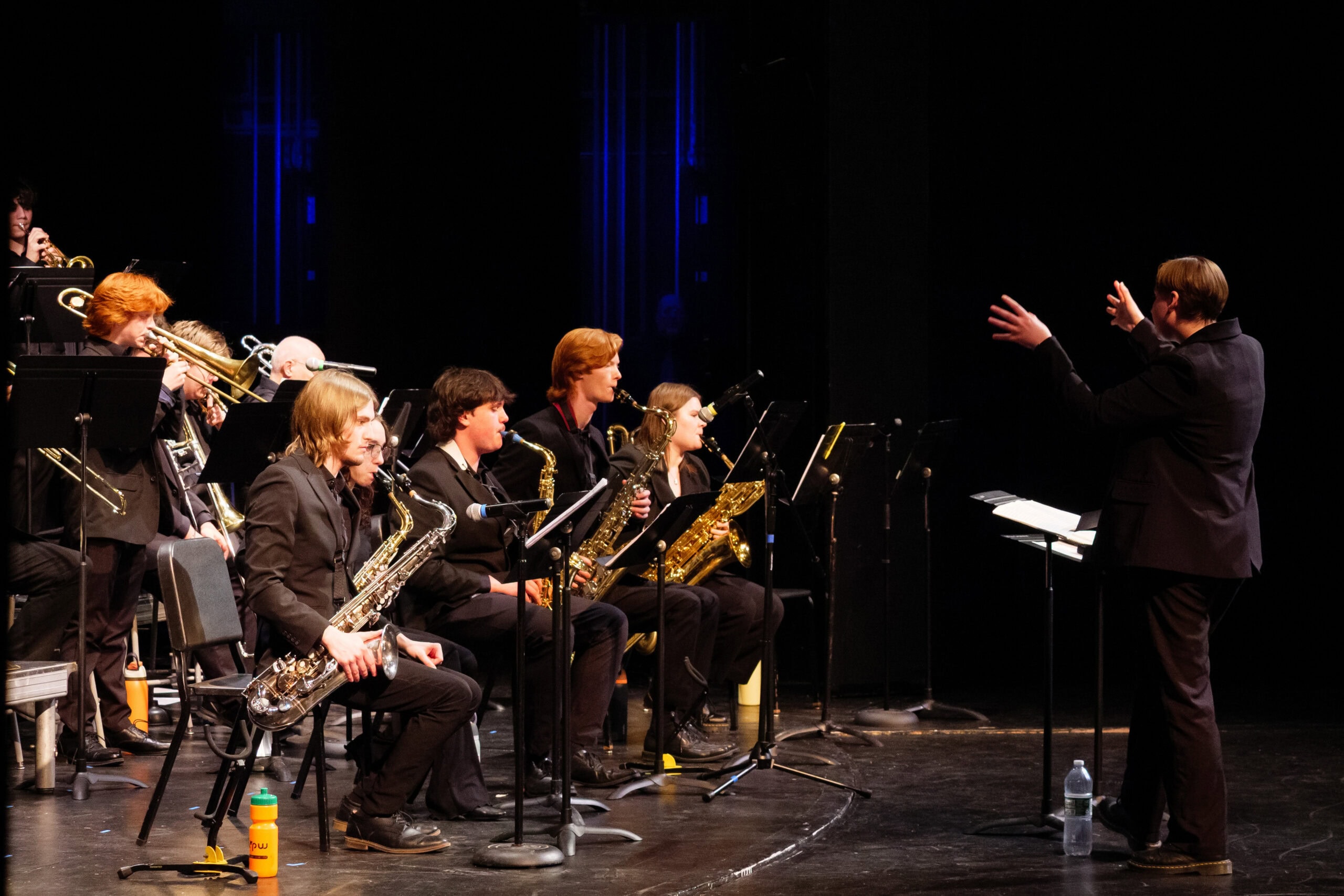 A student in a black suit stands and conducts the Castleton Jazz Ensemble during a performance