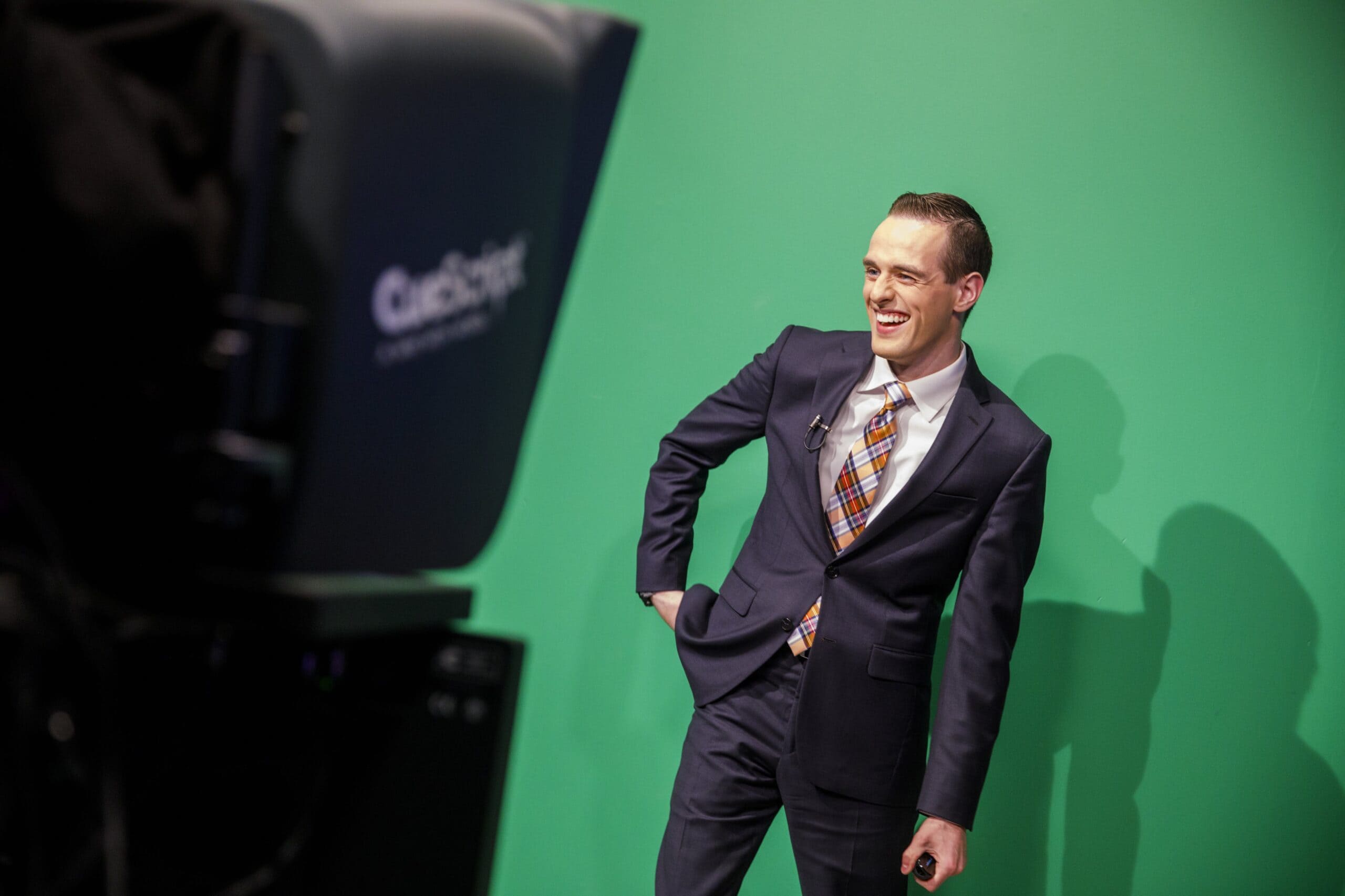 a man in a suit standing in front of a green screen.