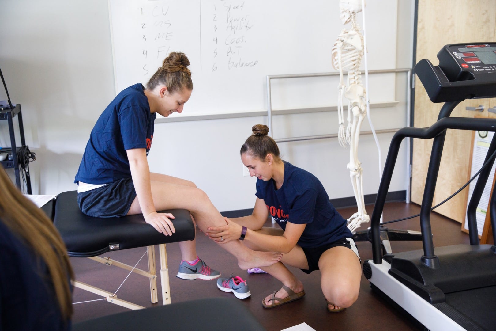 One girl examining the another's leg while studying physical therapy at Vermont State University.