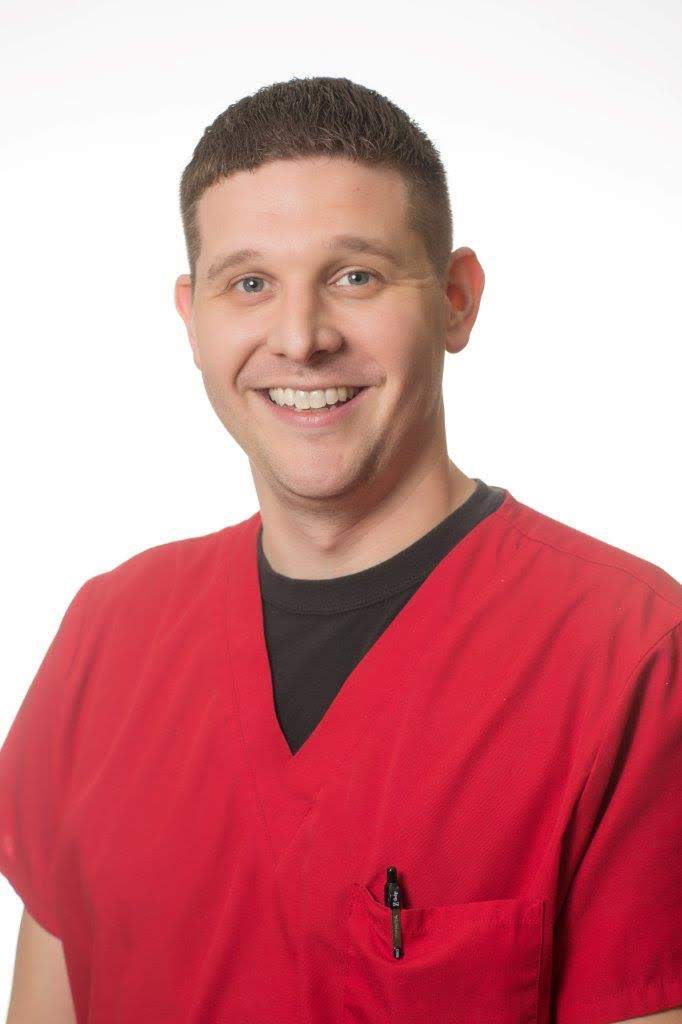 A smiling man in a red scrub shirt.