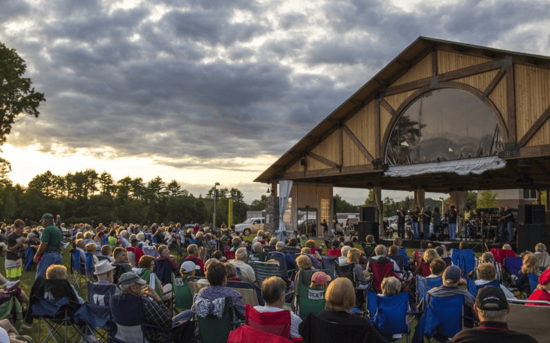 A huge group of people attending a concert outside of a pavilion.