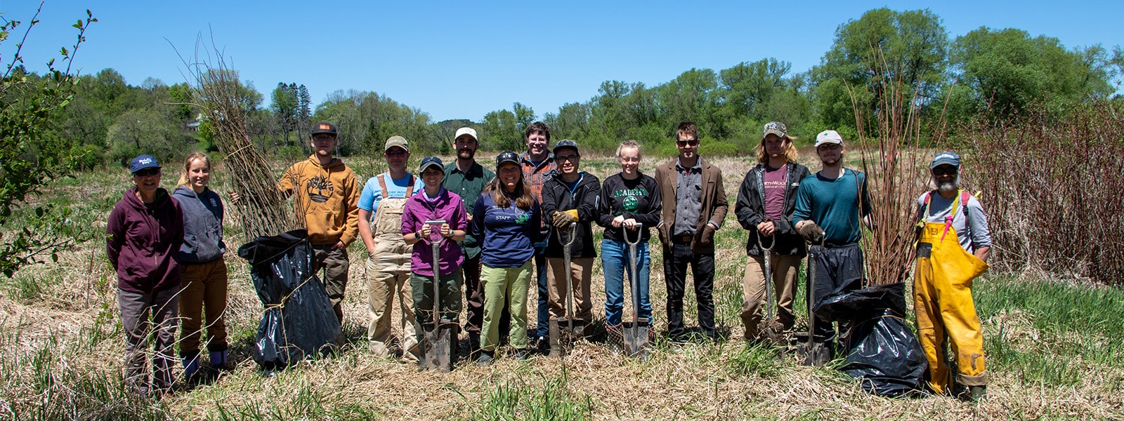 A large group of people stand in a field smiling at the camera.