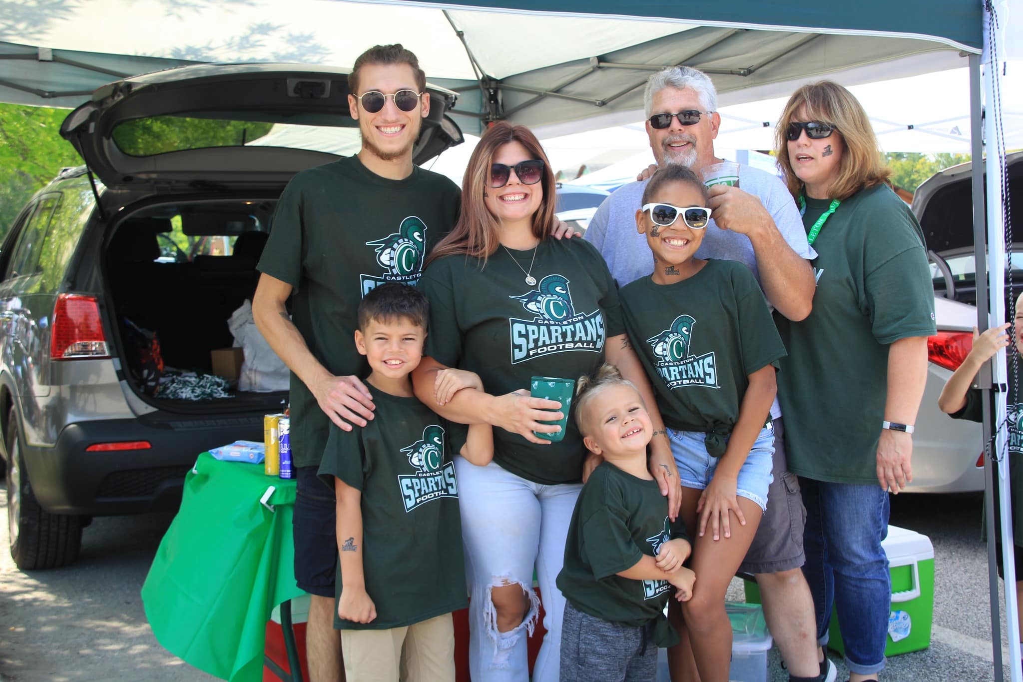 A large family tailgating and smiling at the camera.