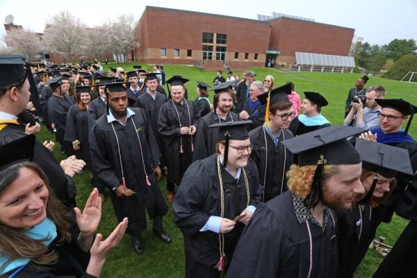 Many students in graduation regalia walking in a line on the Vermont State University Lyndon campus.