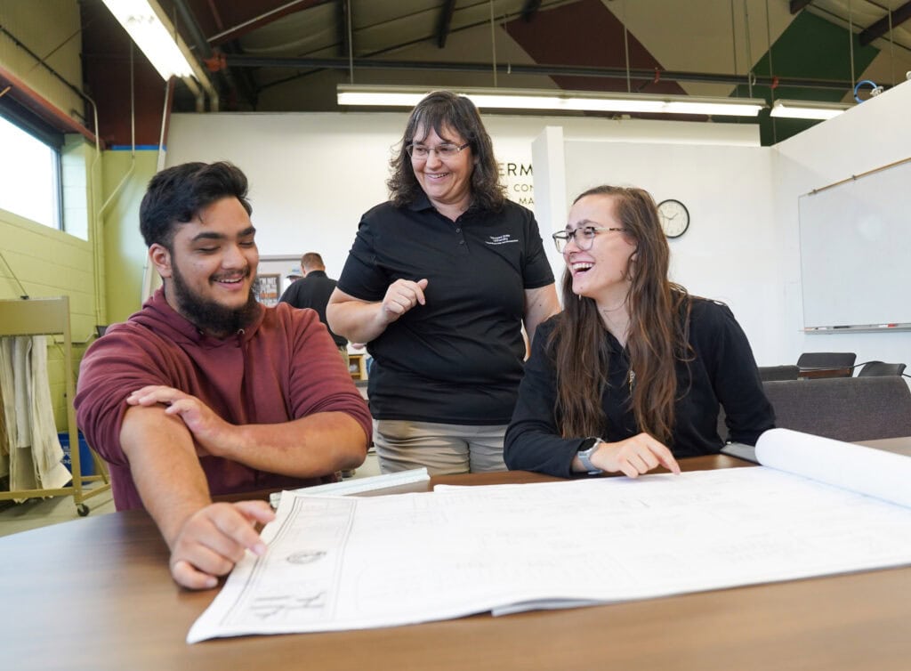 Two students looking over a blueprint and laughing with an instructor at VTSU Randolph