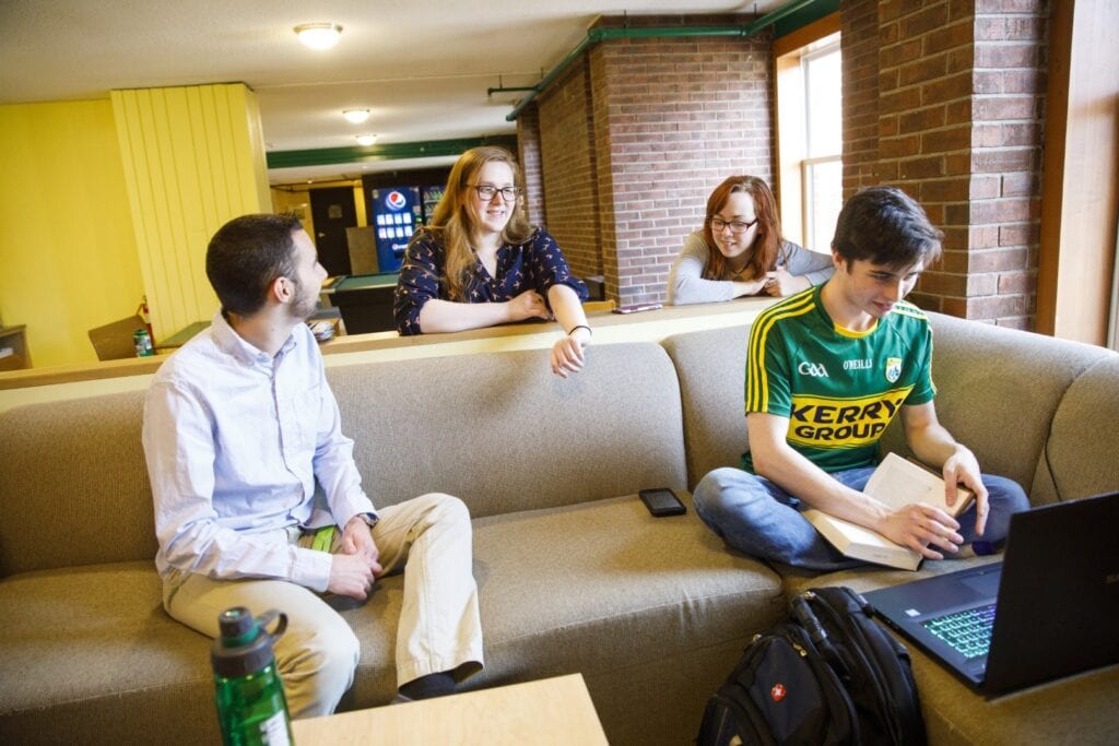 A group of young people gathered around a couch in a residence hall common area.