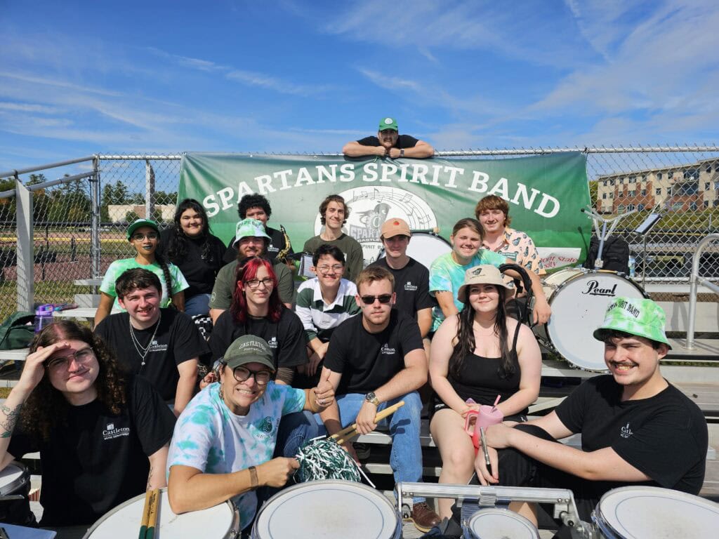Members of the Spartans Spirit Band sitting on metal bleachers at a football game. 