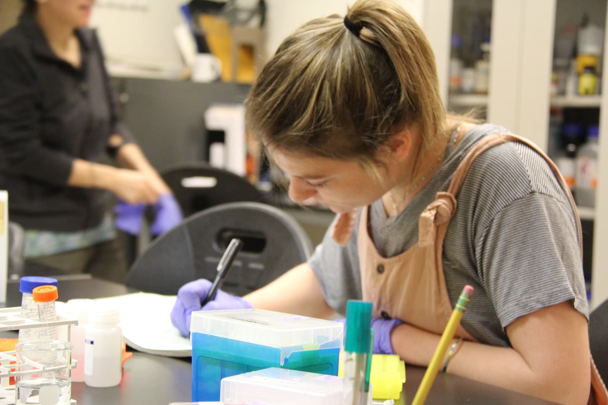 A young girl leans over a notepad writing in a Vermont State University Biology lab.