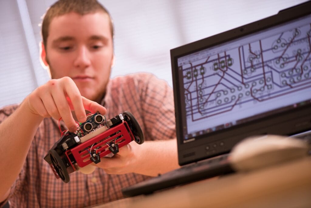 A student in Vermont State University's Electromechanical Engineering program play with a tiny robot.