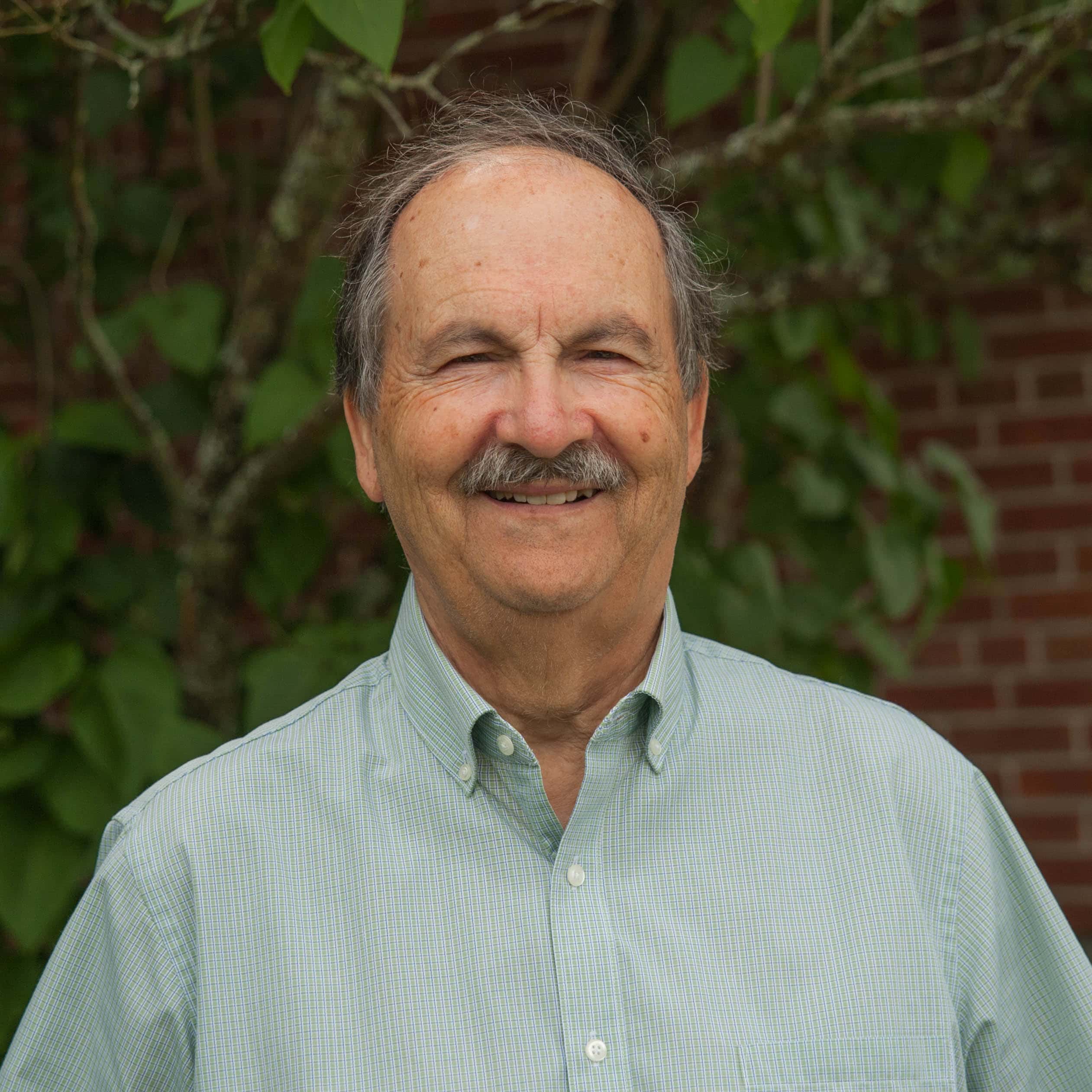 Man in light green shirt smiles at the camera with a brick wall in the background