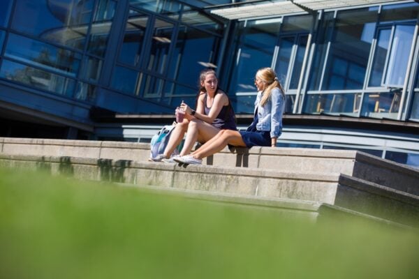 Two girls sitting outside on cement steps at Vermont State University Johnson chatting.