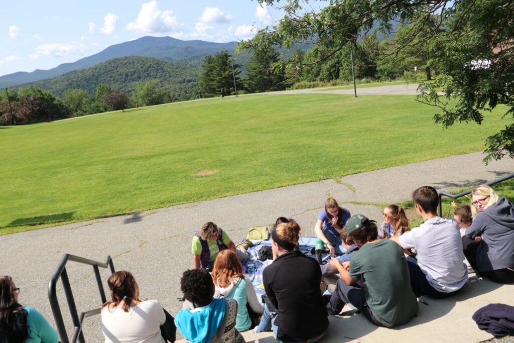 A group of people sitting outside on cement stairs overlooking a green mountain in the distance.