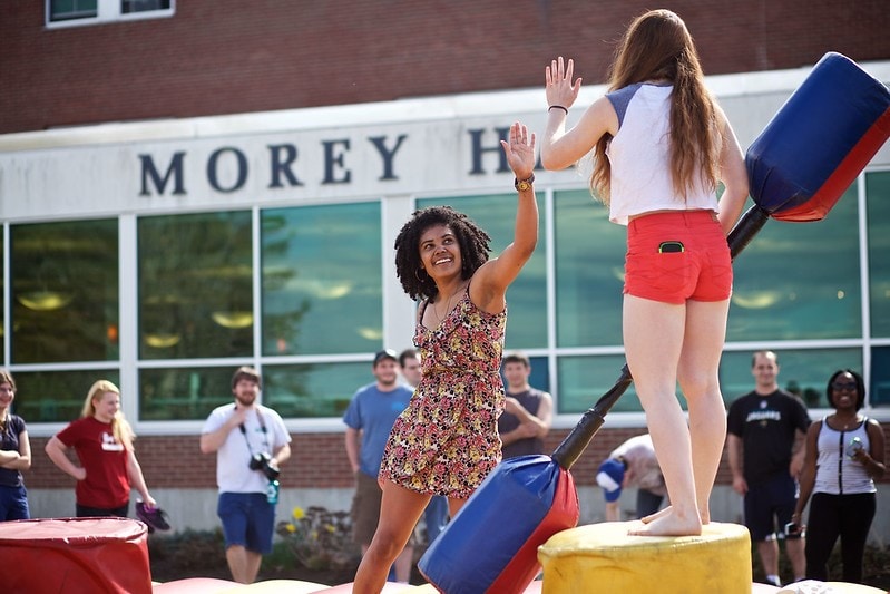 Two girls high-five on a blow-up obstacle course on the Vermont State University Randolph campus.