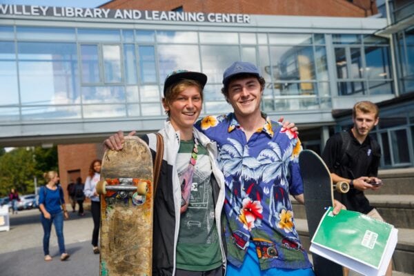 Two young men with skateboards smile at the camera with their arms around each others shoulders on Vermont State Johnson.