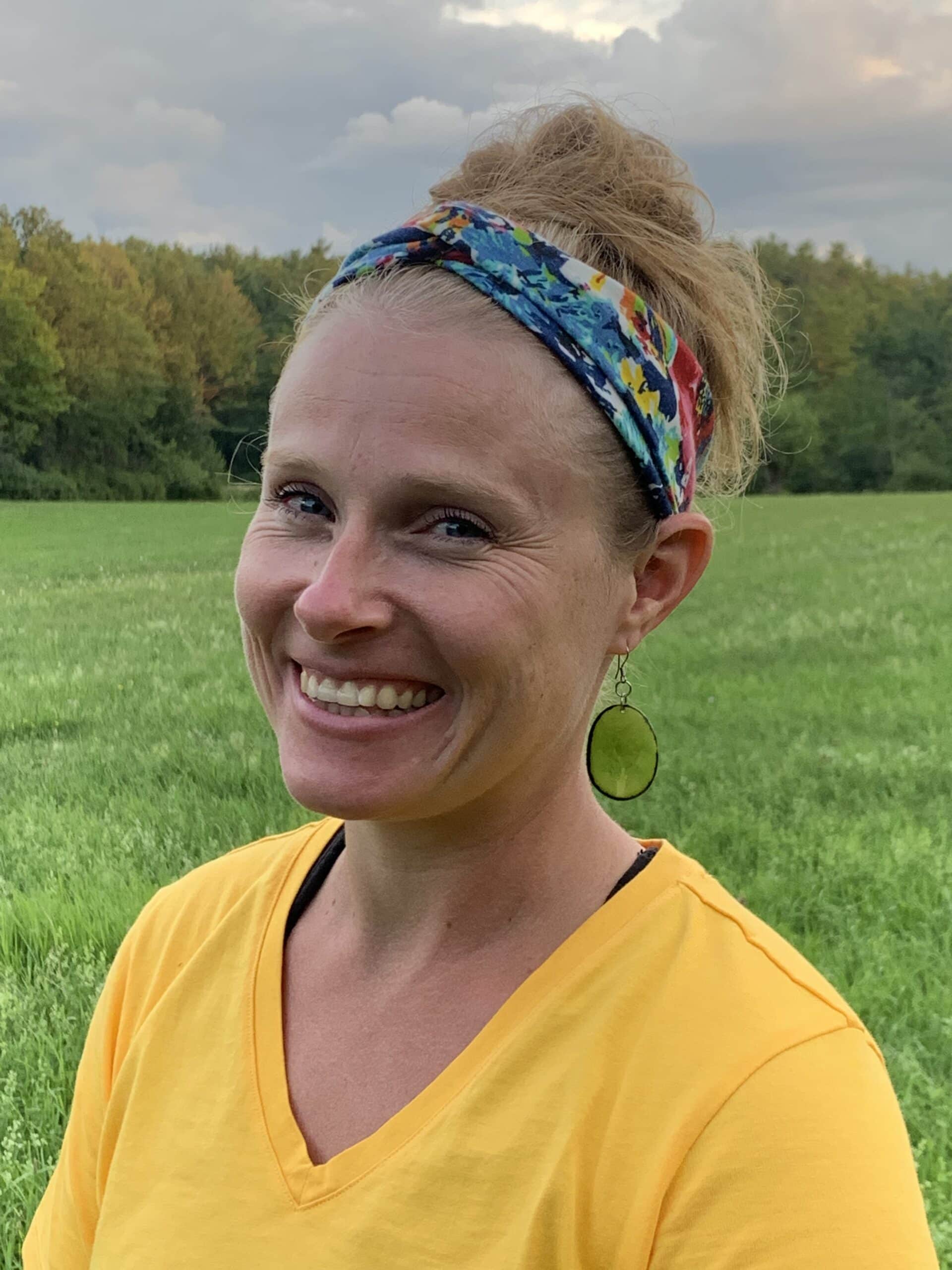 Woman in yellow top smiles at the camera with a field in the background.