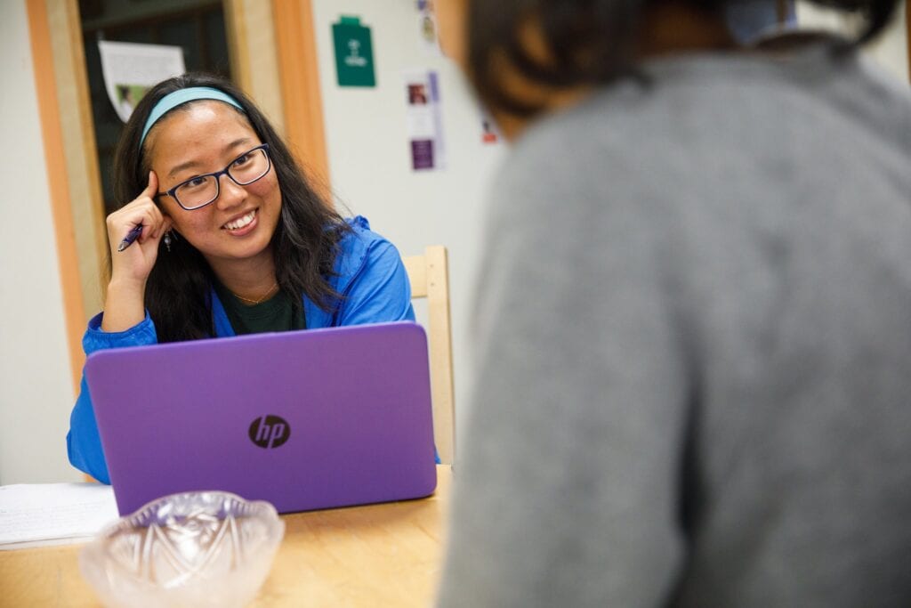 A young girl from Japan smiles over her laptop at Vermont State University.