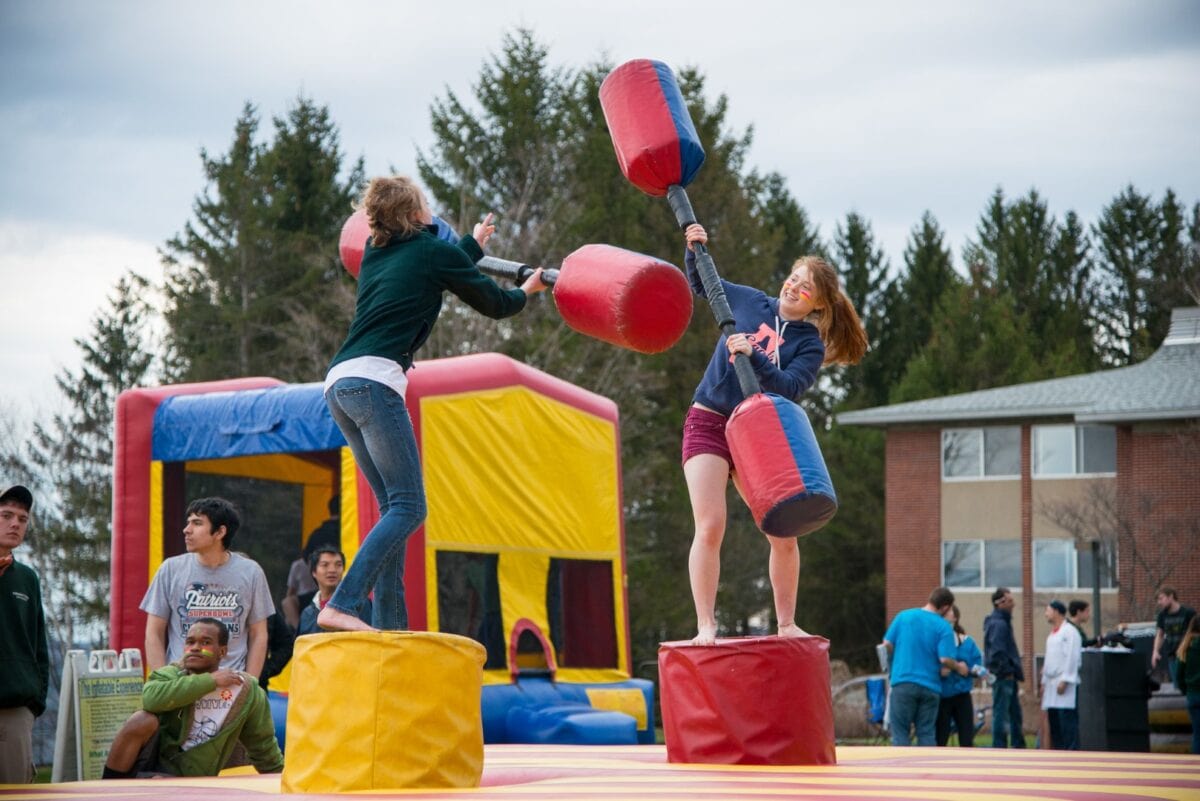 Two girl fight with foam sticks in a blow-up bouncy house outside at Vermont State University Randolph.