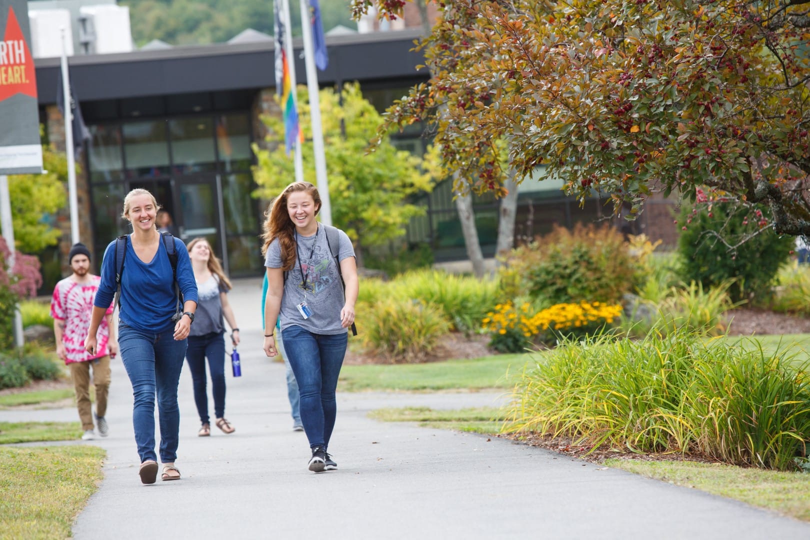 Two young women walking on a paved path in late summer on the Vermont State University Johnson campus.