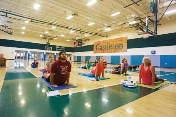 A group of people performing yoga in the Vermont State University Castleton gym.