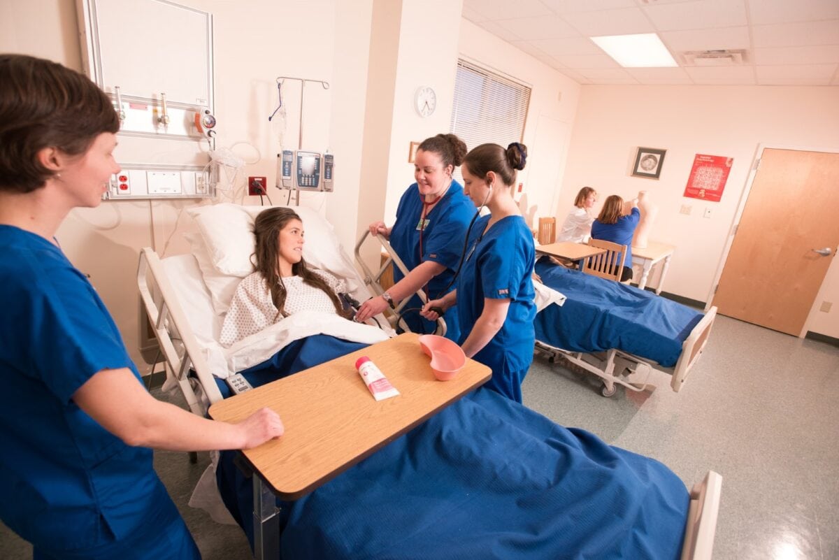 A group of nurses stand around a hospital bed as part of a nursing program at Vermont State University.