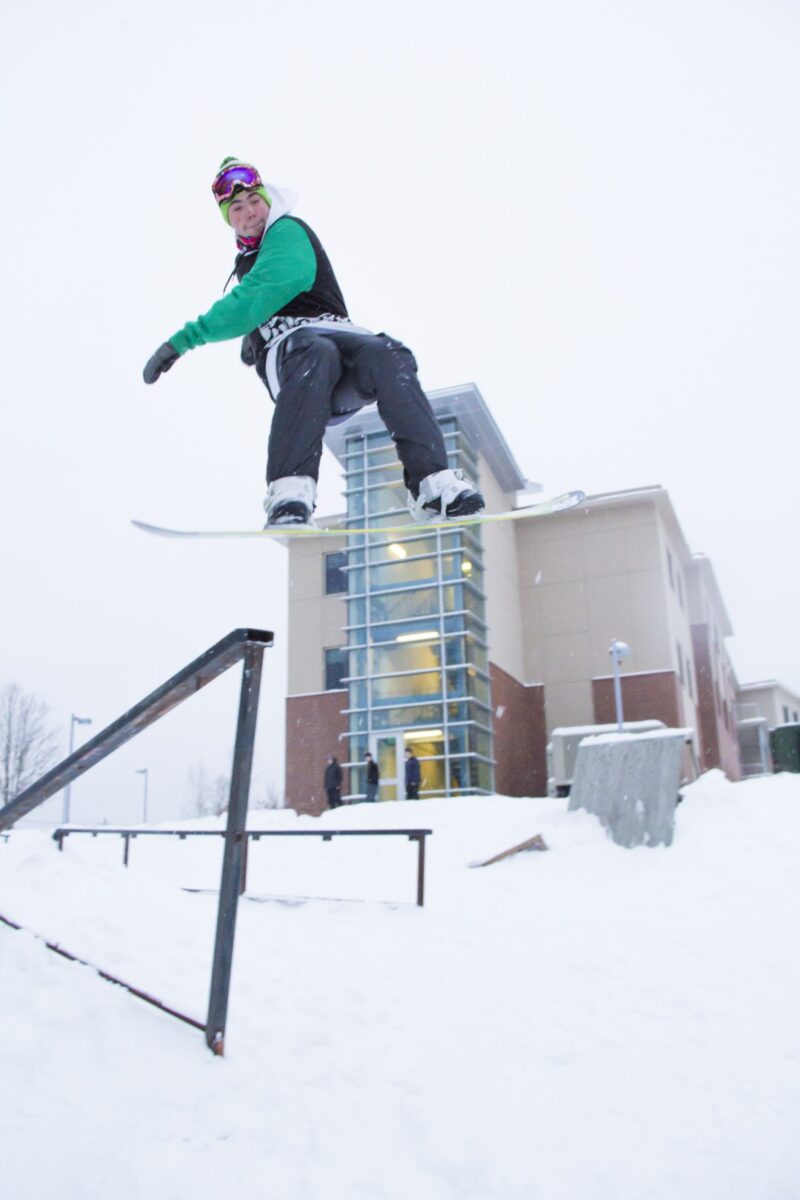 A snowboarder in the air on a snowy afternoon at Vermont State University Castleton.