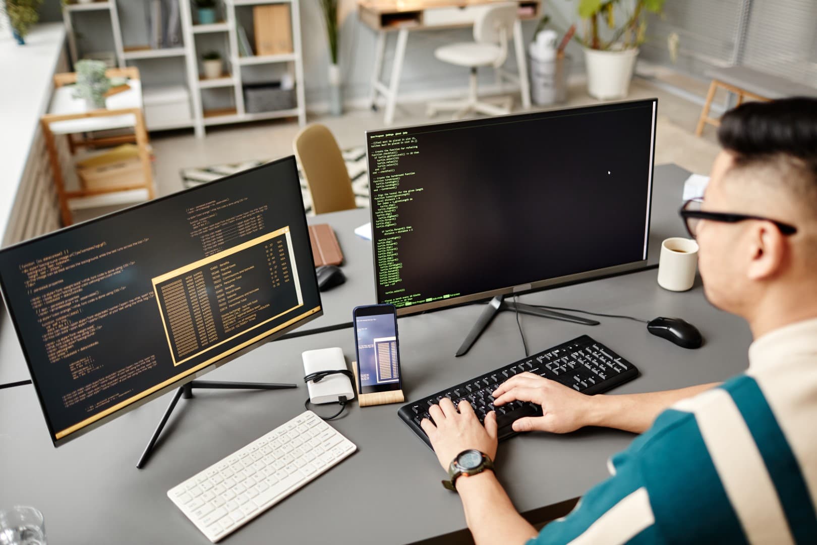 High angle portrait of software engineer typing on keyboard with programming code on computer screen while working in office.